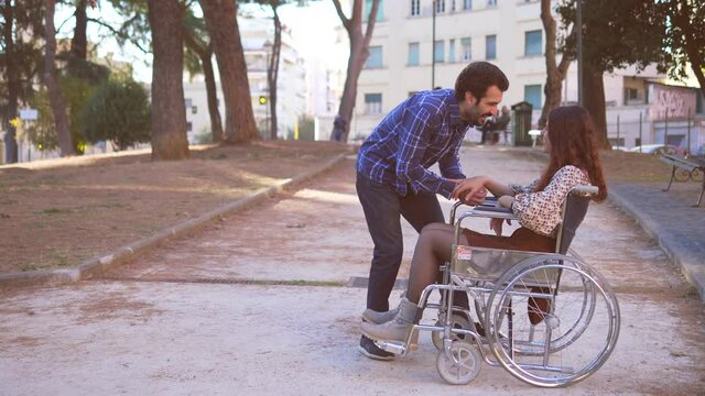 affection, support - young man pays attention to his girlfriend with paraplegia who is waiting for him at the park
