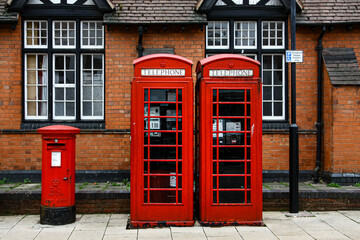 Red telephone boxes and a post box side by side in England, United Kingdom with brick building in the background