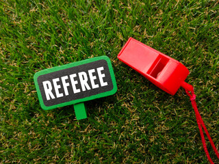 Whistle and colored board written with text REFEREE on a green grass background. Sport and football...