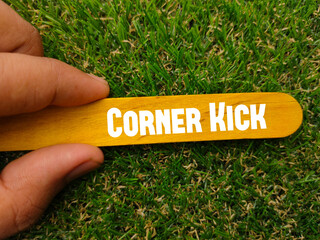 Hand holding colored ice cream stick written with text CORNER KICK on a green grass background....