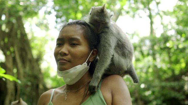 A grey monkey sitting on the shoulders of a shocked and scared young pretty Asian tourist. The macaque is trying to steal her silver necklace and wristwatch