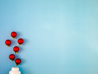 Red Christmas balls like medicine pills blow out or ejection from bottle on blue background. Top view, flat lay, copyspace. Medical banner concept new year or Christmas. Winter holidays in pandemic.