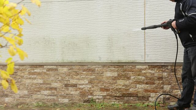 Man cleaning walls with high pressure power washer. Washing cladding walls house.