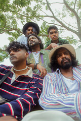Malaysian Indian men in a group against a cloth backdrop in a park surrounded by trees, talking,...