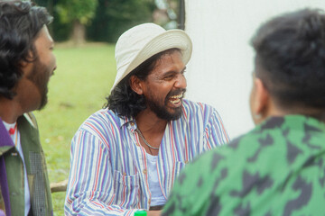 Malaysian Indian men in a group against a cloth backdrop in a park surrounded by trees, talking,...