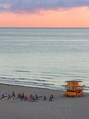 A group of people completing yoga class on South Beach Miami at sunrise next to a lifeguard hut.