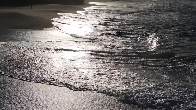 Sunset sunlight reflecting on the wave-wet beach sand