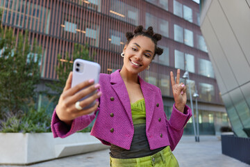 Attractive girl in fashionable outfit creats influence content shows peace sign at smartphone front...