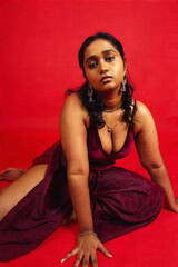 Malaysian Indian individual dressed in red clothing, against a red background, posing and laughing