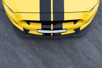 The hood of a yellow car with black stripes. View from above. Asphalt background