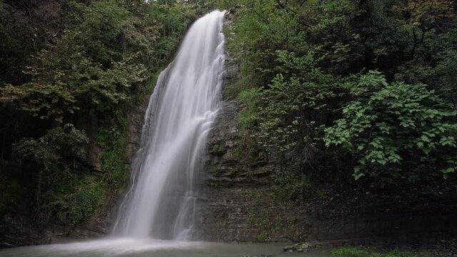 Time lapse featuring big waterfall flowing into the stream while it's raining. Zoom out.