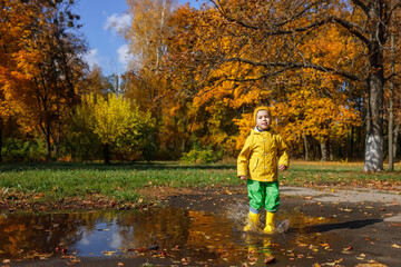 smiling child boy in yellow raincoat have fun with puddle