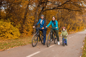 family with child riding on bikes together in autumn park