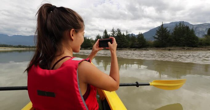 Kayak. Woman using phone taking pictures kayaking in Squamish Estuary surrounded by mountains relaxing enjoying tranquility. People living healthy active outdoor life in British Columbia, Canada.