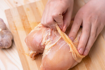 Chef's hands peeling raw chicken breast