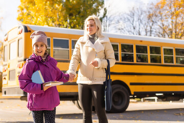 Mother and her daughter next to school bus in the morning