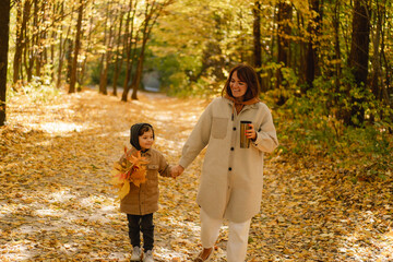 Fototapeta premium Happy young mother and son are walking in the autumn forest. Autumn outdoor activity for family with kids. Happy mother's day. Family day. Autumn day. Happy family leisure.