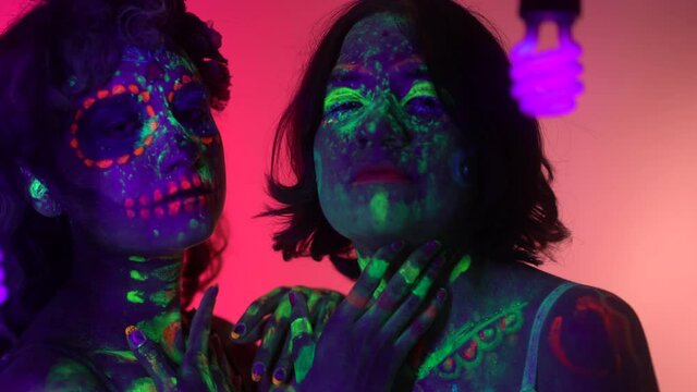 Neon Halloween make up for Day of the Dead celebration in Mexico. Ultra violet neon portrait photography with two hispanic girls. 