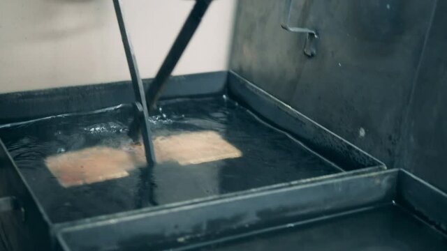 A bar of gold is getting relocated between trays with liquid
