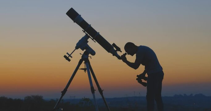 Silhouette of a man, telescope under the starry skies.	

