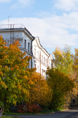 Urban autumn landscape. An old white house covered with trees in colorful autumn foliage.
