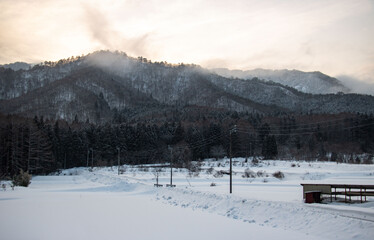 Fototapeta na wymiar 日本の田舎の雪景色　夕焼けと雪山と雪が積もる畑と一本道