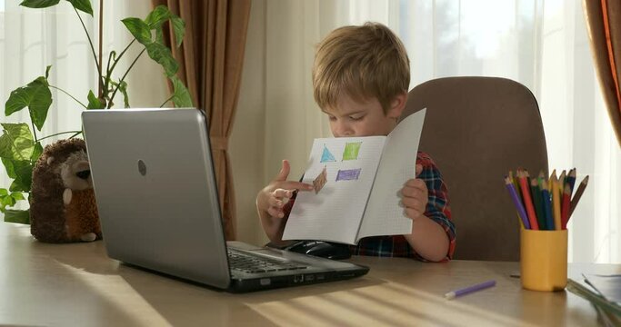 Child Study Online Lesson Video Conference Chat Using Laptop Computer. Kid Distance Learning at Home. Preschooler Boy Sits at Desk Table in Room Near Window 4K