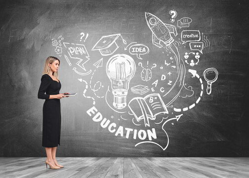 Side view of attractive businesswoman in formal black dress and high heels standing nearby chackboard wall with drawn educational sketches and pondering about education to start new business