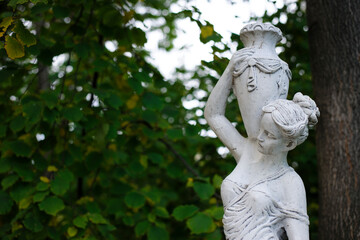 Fototapeta na wymiar sculpture of a girl in the spring park. An old statue in a park of a sensual semi-nude Greek or Italian Renaissance woman with a vase in a city park. sunny day in the summer garden. close-up