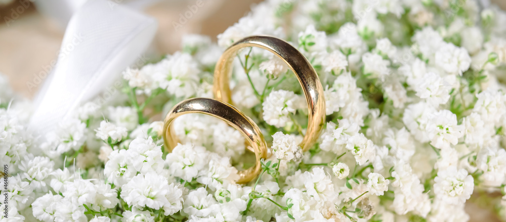 Wall mural wedding rings lie on a beautiful bouquet white as bridal accessories - wedding rings stand on white and green flower bouquet - close up - banner - Wall murals