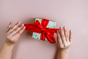 Female hands holding gift box on beige background. Present for Christmas, New Year, Valentine Day. Top view