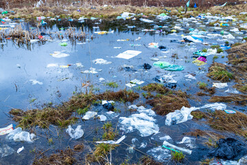 Verkhnie-Sergi, Russia - May 02, 2021. a lot of garbage and plastic bags in a puddle of water on the field. grass and packages. danger of pollution of the environment