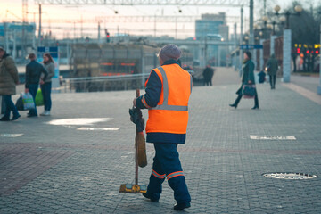 Female municipal worker cleaning railway station. Cleaner sweeping pedestrian zone at train station...