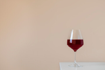 Glass of red wine on white table on beige neutral background with space for text, simple elegant composition
