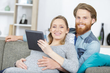 expectant couple on sofa looking at tablet pc