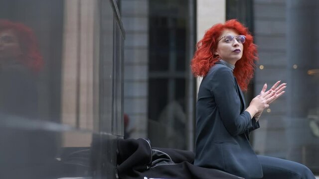 stylish business woman with red hair in a suit sitting on the street