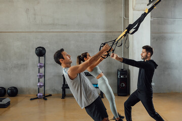 Personal trainer coaches clients to work out using suspension training straps.