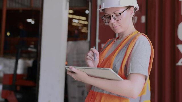 Confidence female warehouse staff using digital tablet working and at shipping dock of logistic distribution center