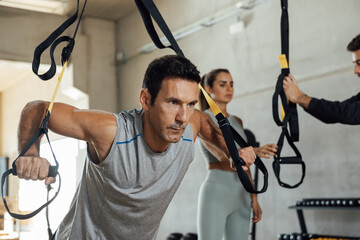 Fit man trains push ups with suspension trx straps at gym club.