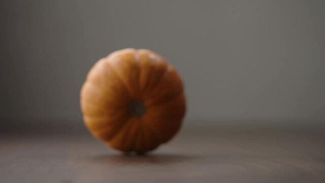 Slow motion small orange pumpkin rolling in frame on walnut table with copy space