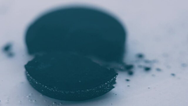 Close-up of a black tablet dissolving in water. Medical background in soft focus at high magnification. Activated charcoal in the form of a pill.