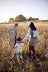 family of three with a boy child mom and dad are standing on a field in autumn at sunset