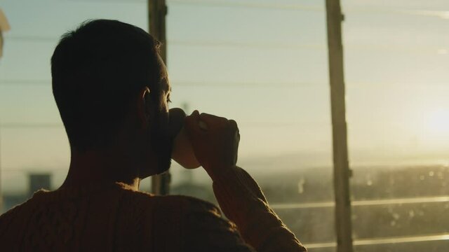 Sagoma di un uomo che beve una tazza di the alla finestra al tramonto.