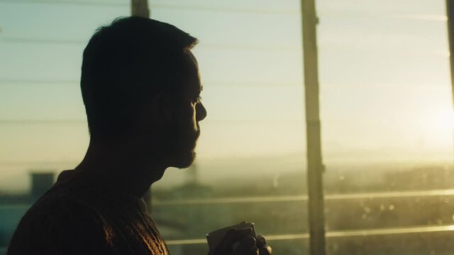 Sagoma di un uomo che beve una tazza di the alla finestra al tramonto.