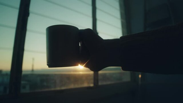 Sagoma di un uomo che beve una tazza di the alla finestra al tramonto.