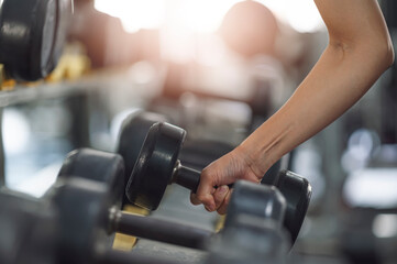 Plakat Close-up female hands lifting dumbbells at gym.