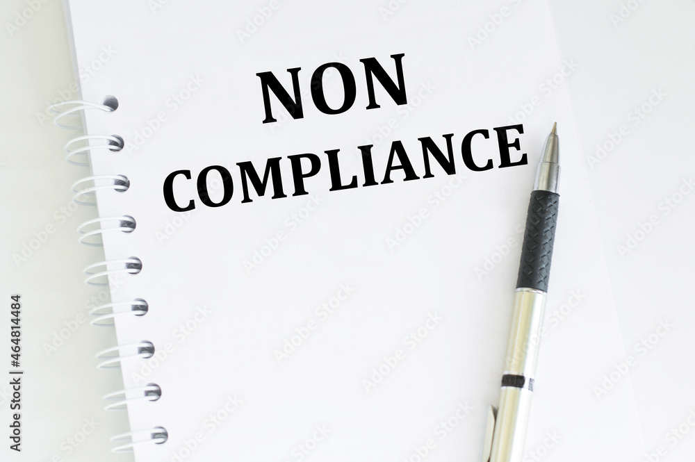 Poster text non compliance on a white notebook next to the handle on a light table