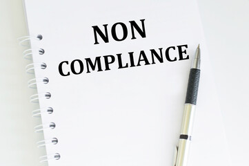 text NON COMPLIANCE on a white notebook next to the handle on a light table