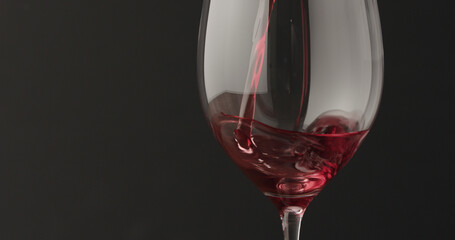Obraz na płótnie Canvas pour red wine into wineglass over black baground