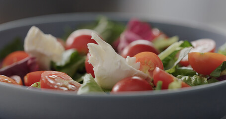 mozzarella over mixed greens into blue bowl, making salad